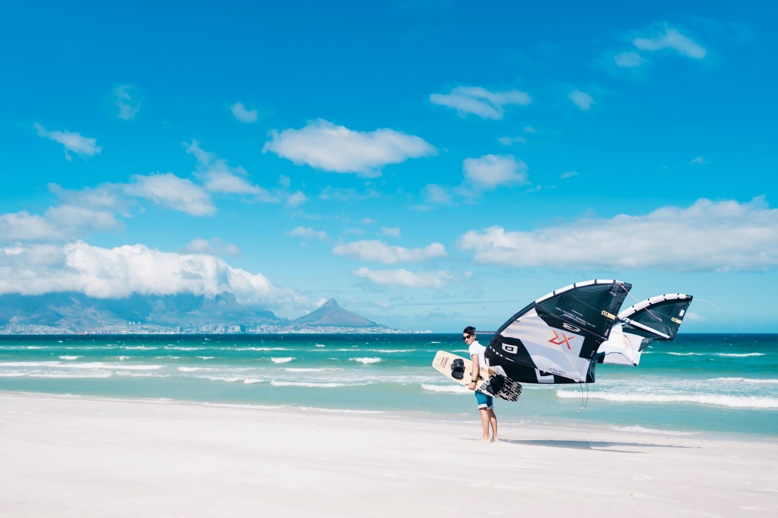 A kiter carrying kite and board on Blouberg beach with Table Mountain behind